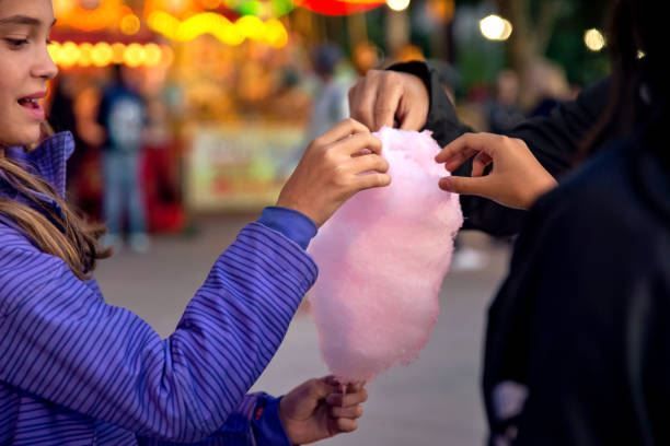 Two people sharing pink cotton candy at a colorful fairground stall