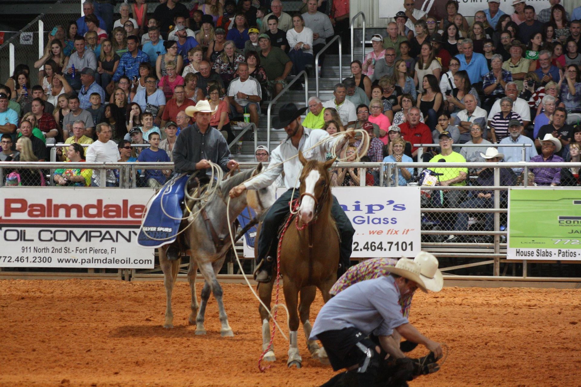 Cowboy on a bucking horse in a rodeo arena, with a photographer crouched in front and a crowd behind