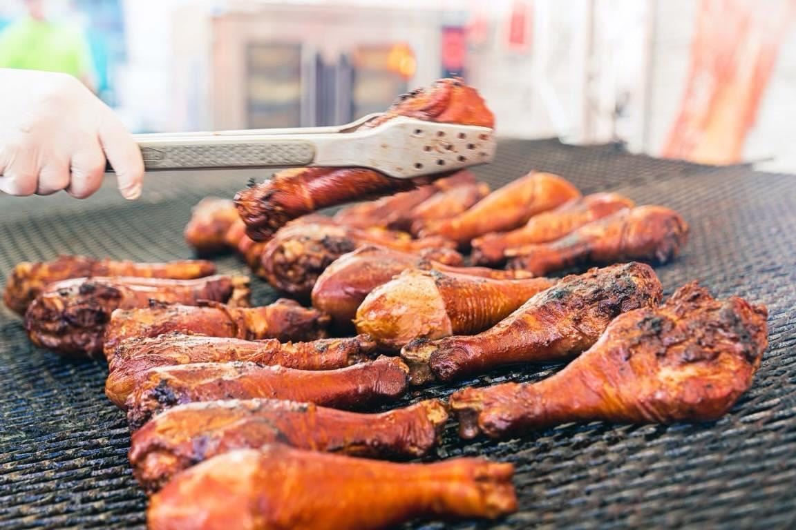 Grilled chicken drumsticks on a barbecue grate, with a hand using tongs to turn them.