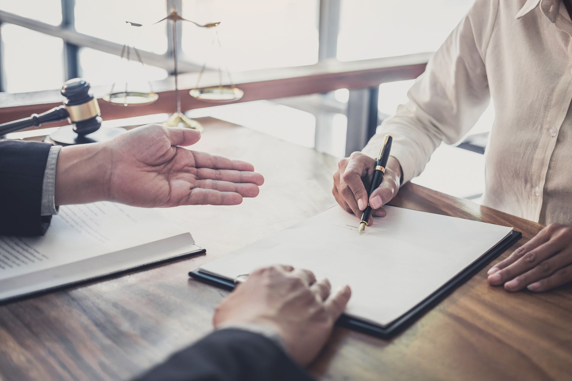 Two People at A Desk, One Signing a Document with A Pen While the Other Gestures — SouthMac Finance In Townsville, QLD