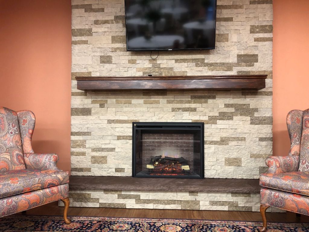 A living room with a fireplace , chairs and a flat screen tv.