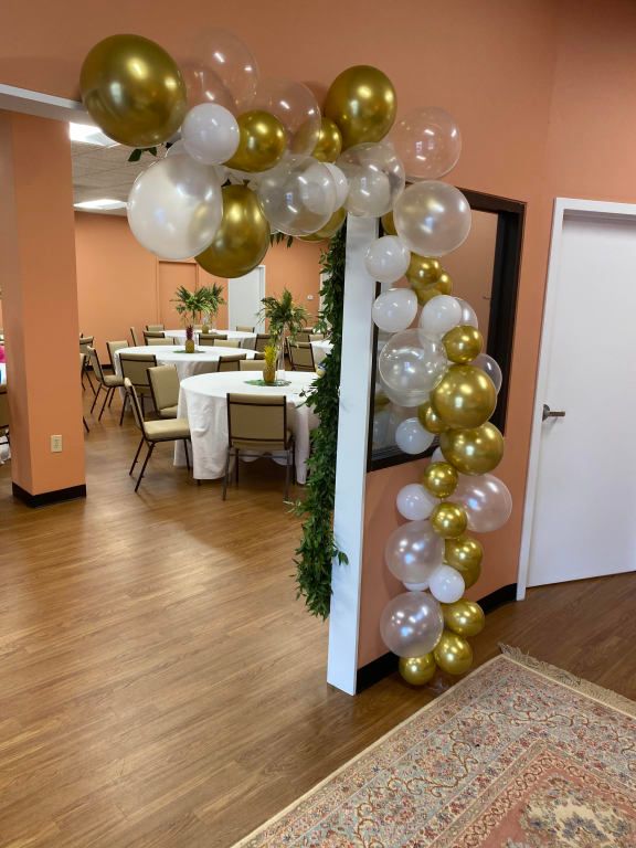 A room with tables and chairs decorated with gold and white balloons
