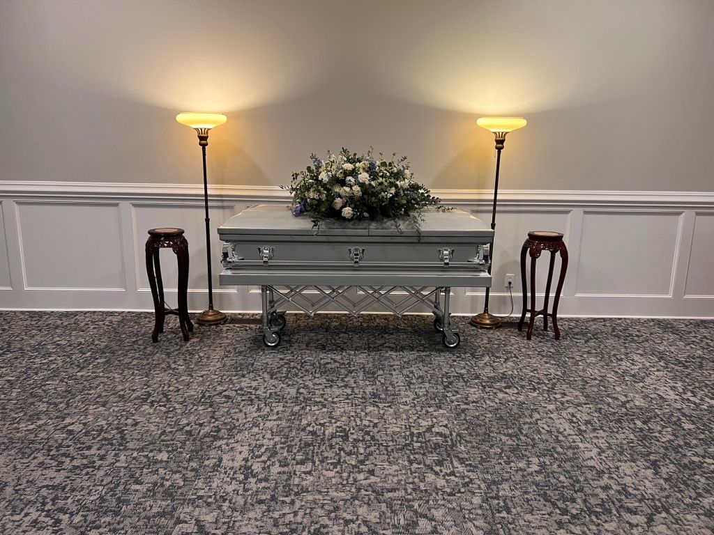 A white coffin is sitting on a table in a room with two lamps.