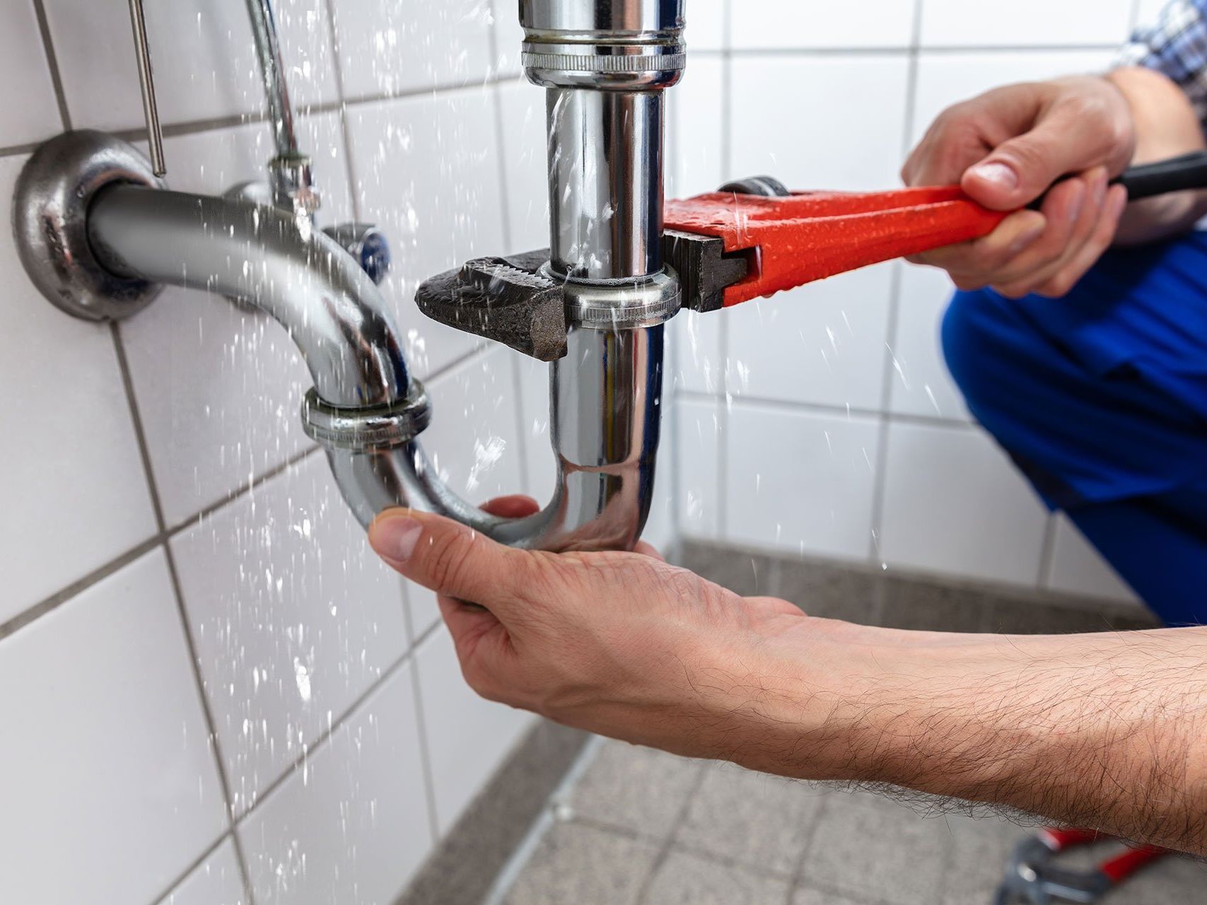 A plumber is fixing a pipe with a wrench in a bathroom.