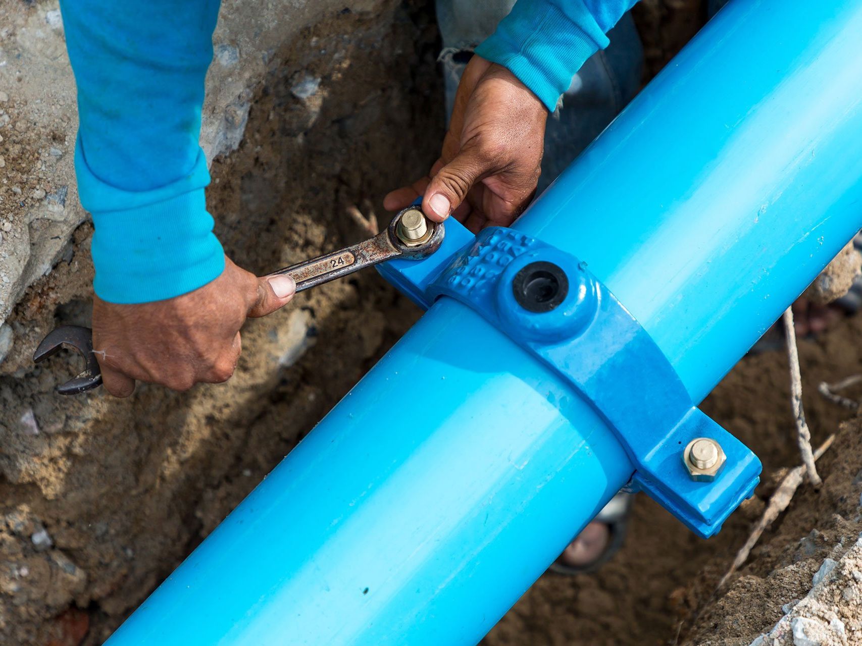 A man is fixing a large water main pipe with a wrench.