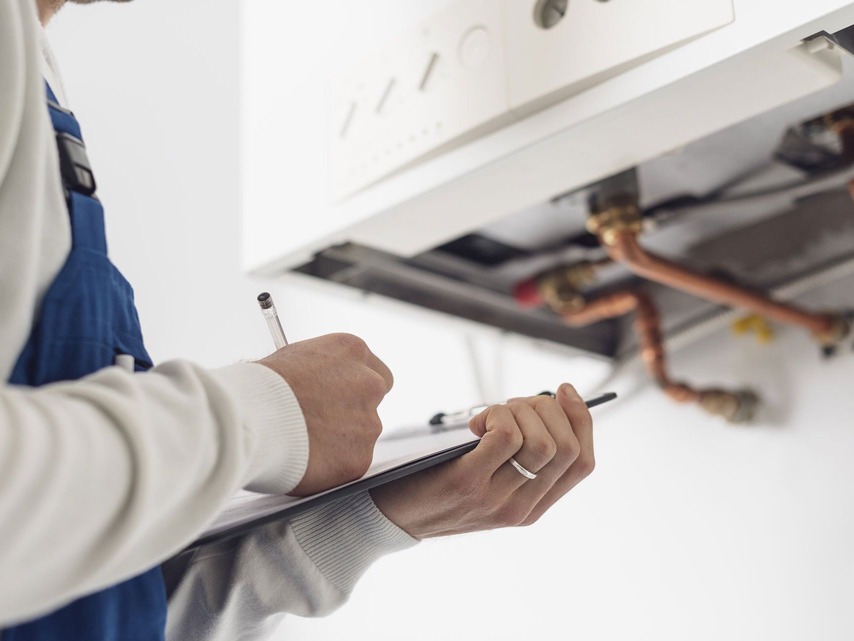 A man is writing on a clipboard in front of a boiler.