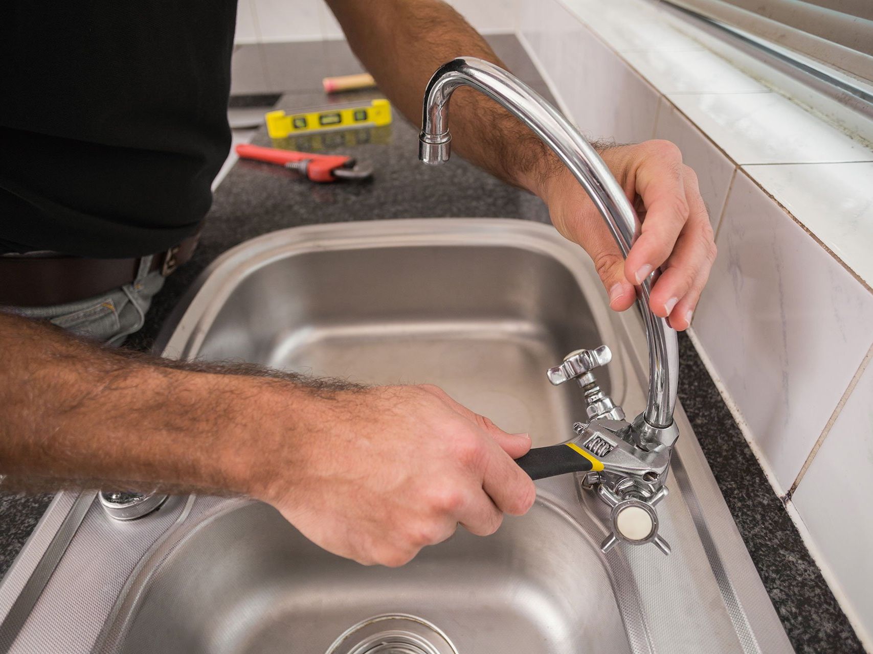A man is fixing a faucet in a kitchen sink with a wrench.