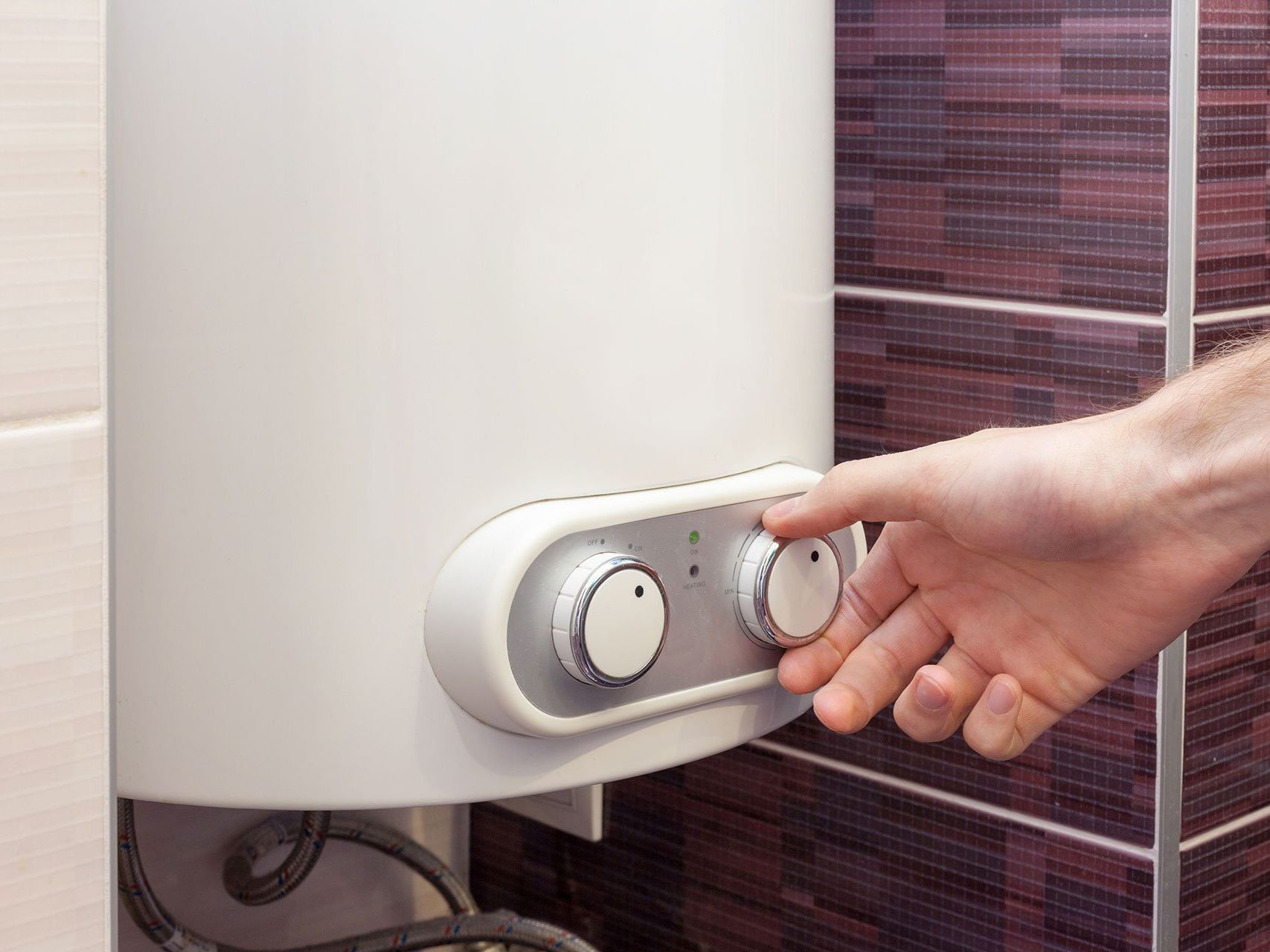 A person is adjusting the temperature of a water heater in a bathroom.