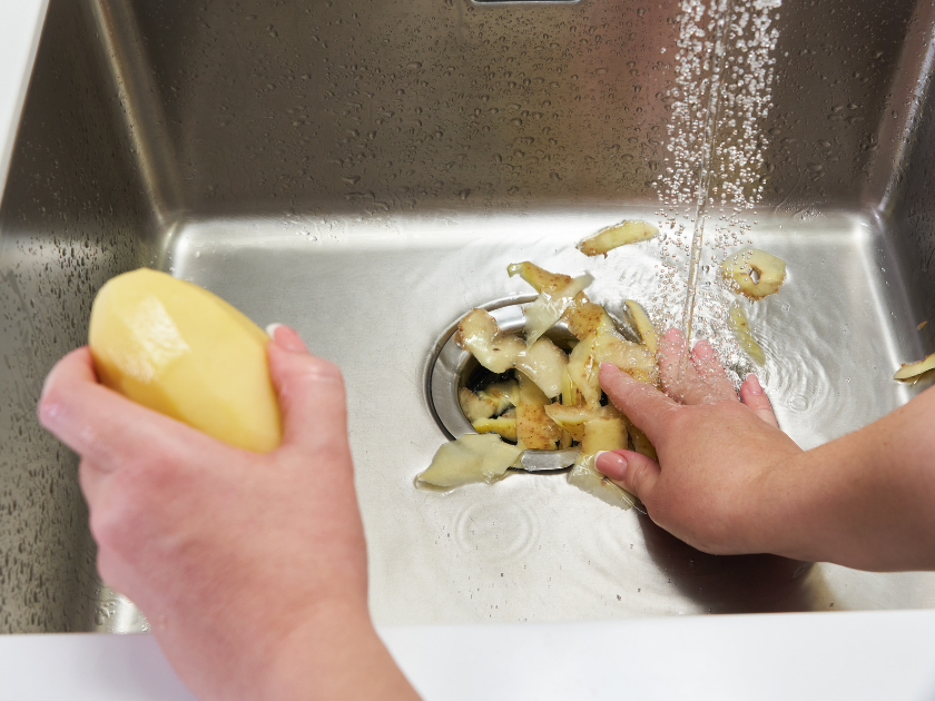 A person is peeling a potato in a sink.
