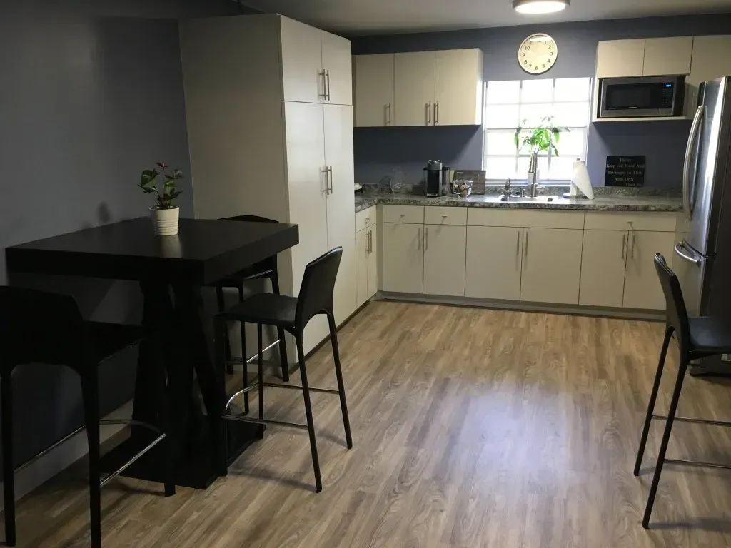 Small modern kitchen and dining area with black table, chairs, white cabinets, and wood floor.