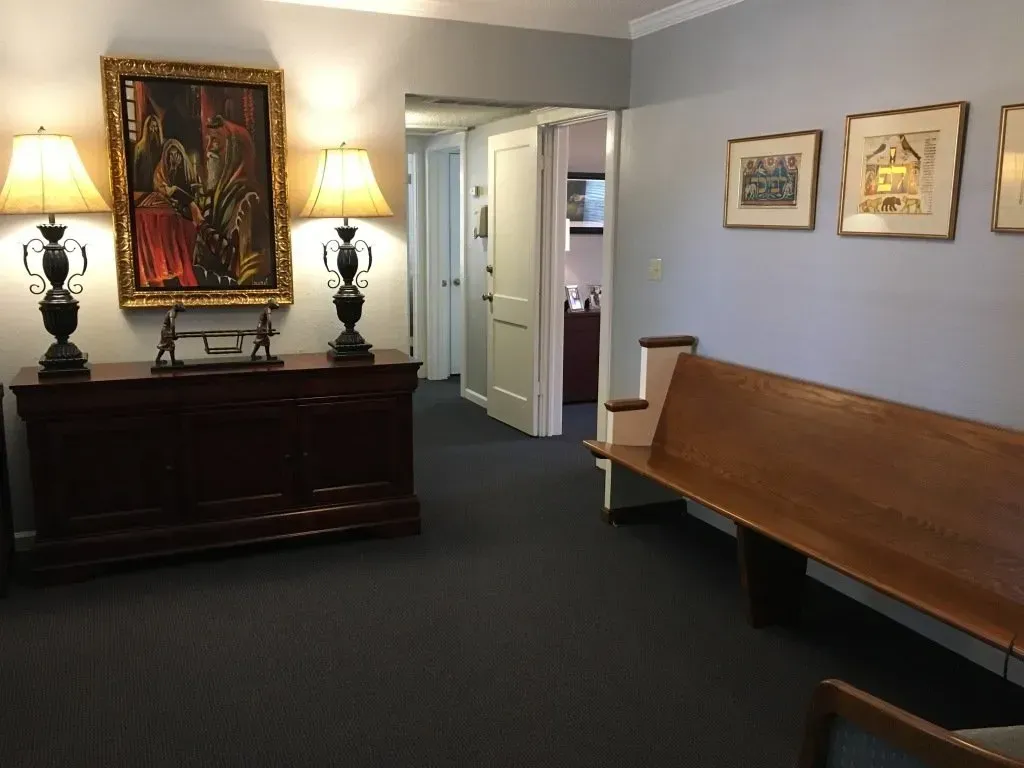 Office hallway with dark bench, lamps, framed art, and a doorway in the back