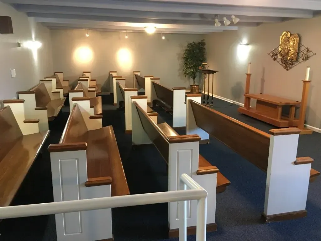 Empty church pews facing the altar in a small chapel with blue carpet and white walls