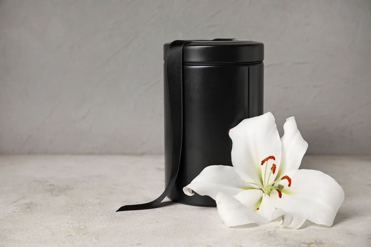 Black cylindrical container beside white lily flowers on a gray surface.