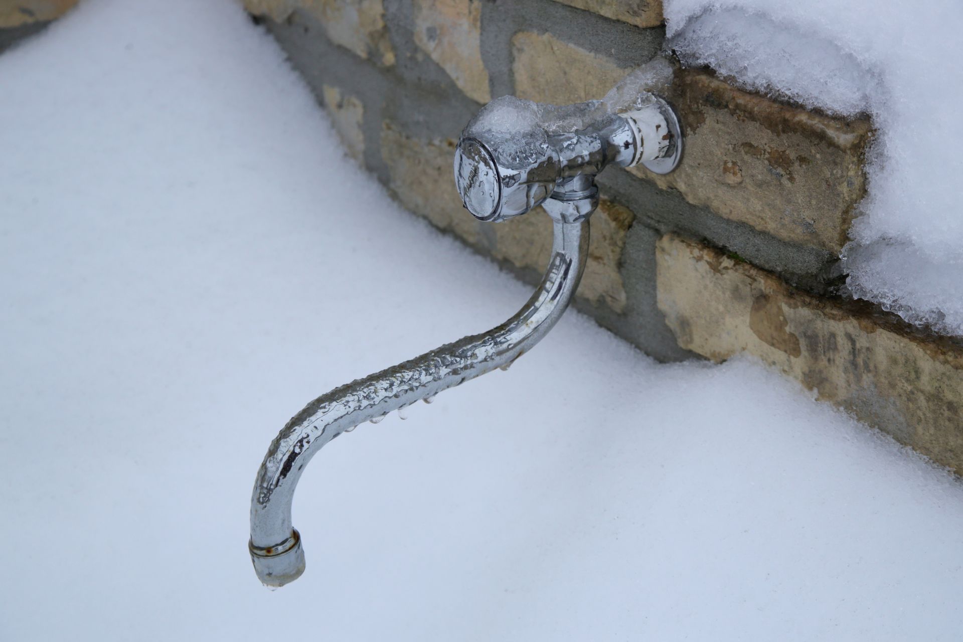 An outdoor metal water faucet covered in ice and snow, attached to a stone wall. An outdoor metal water faucet covered in ice and snow, attached to a stone wall.