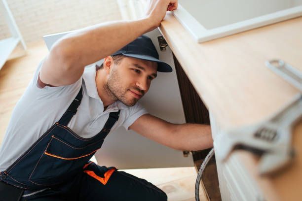 Professional plumber repairing kitchen sink pipe with wrench and tools on wooden countertop.
