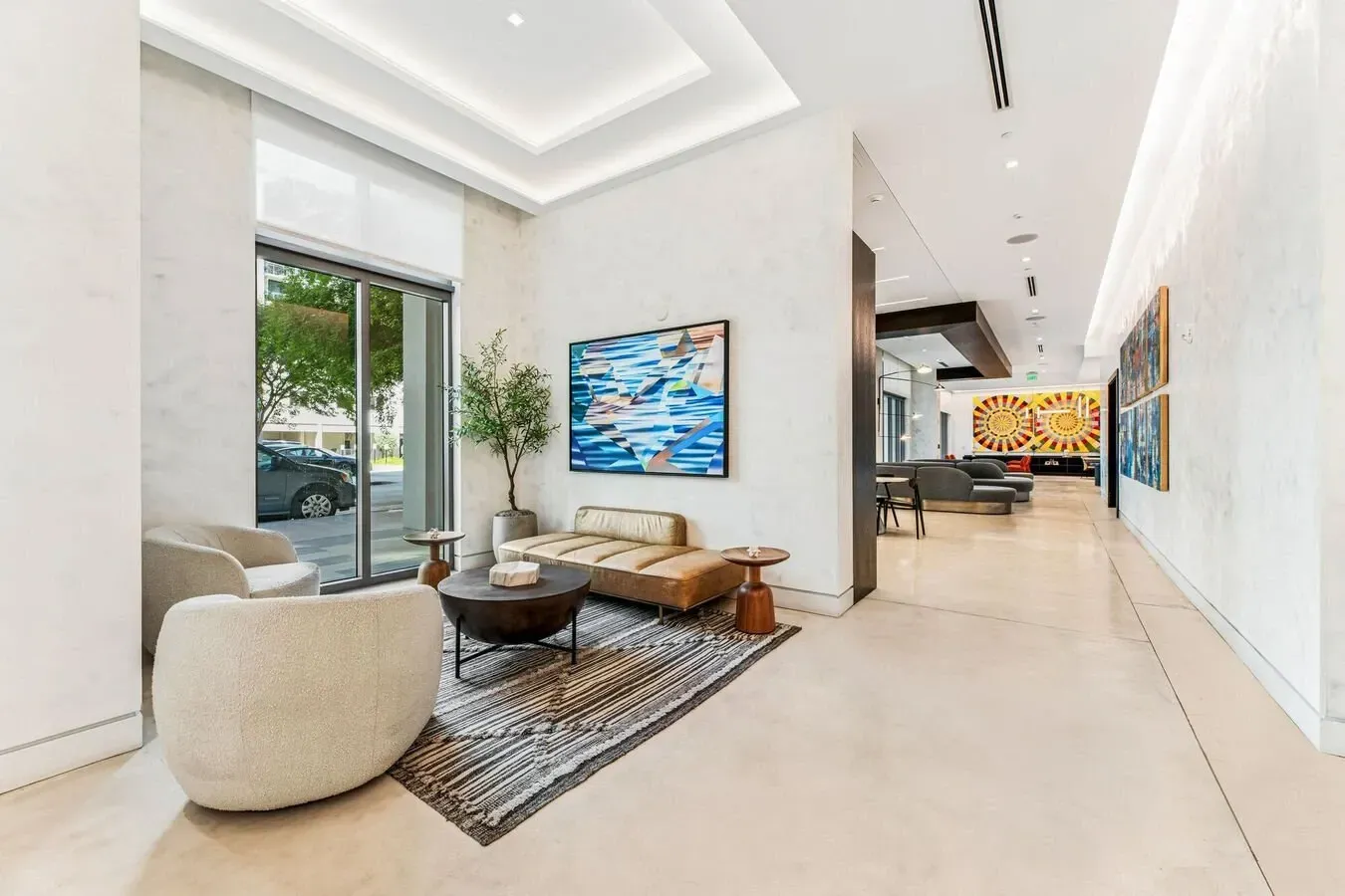 Modern living room with beige seating, abstract wall art, and large windows opening to greenery