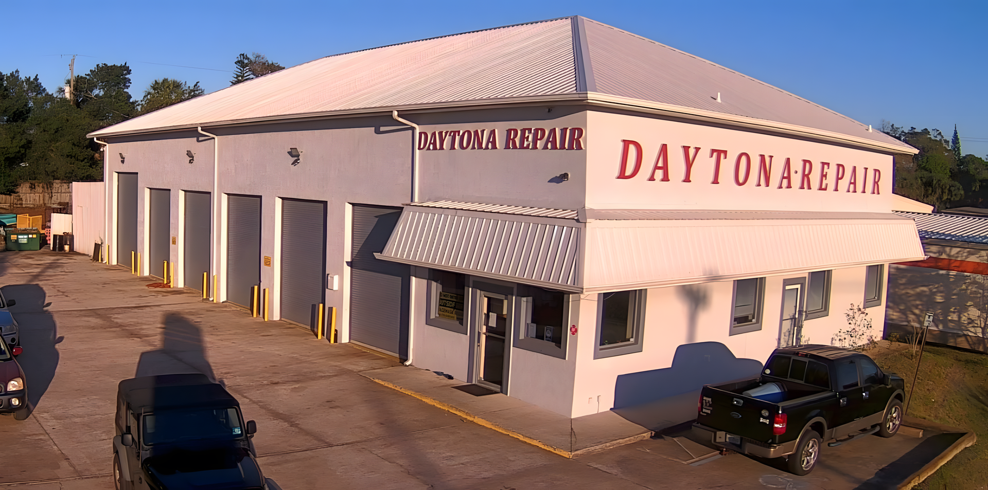 Daytona Repair auto shop with garage doors, red lettering, and a black pickup truck | Daytona Automotive