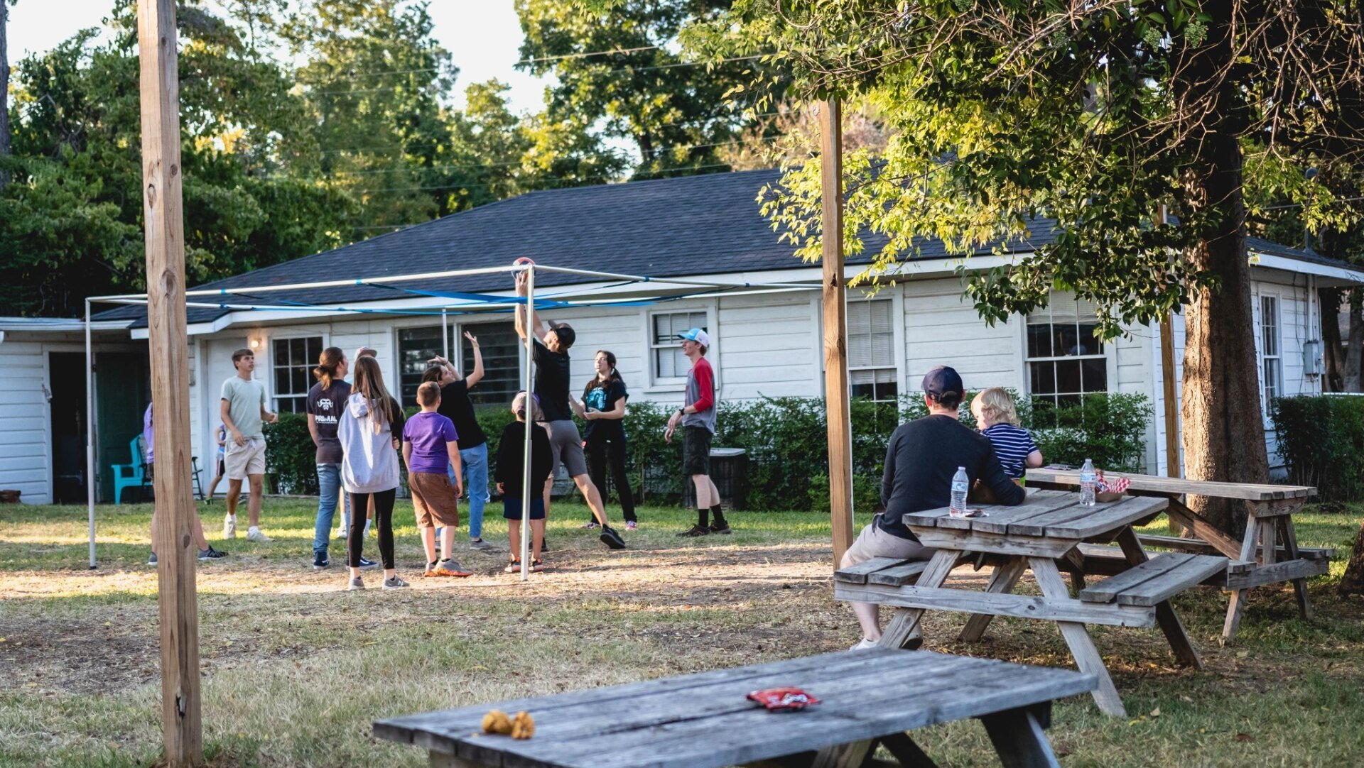 Group of people playing a game in a backyard; white house in background.