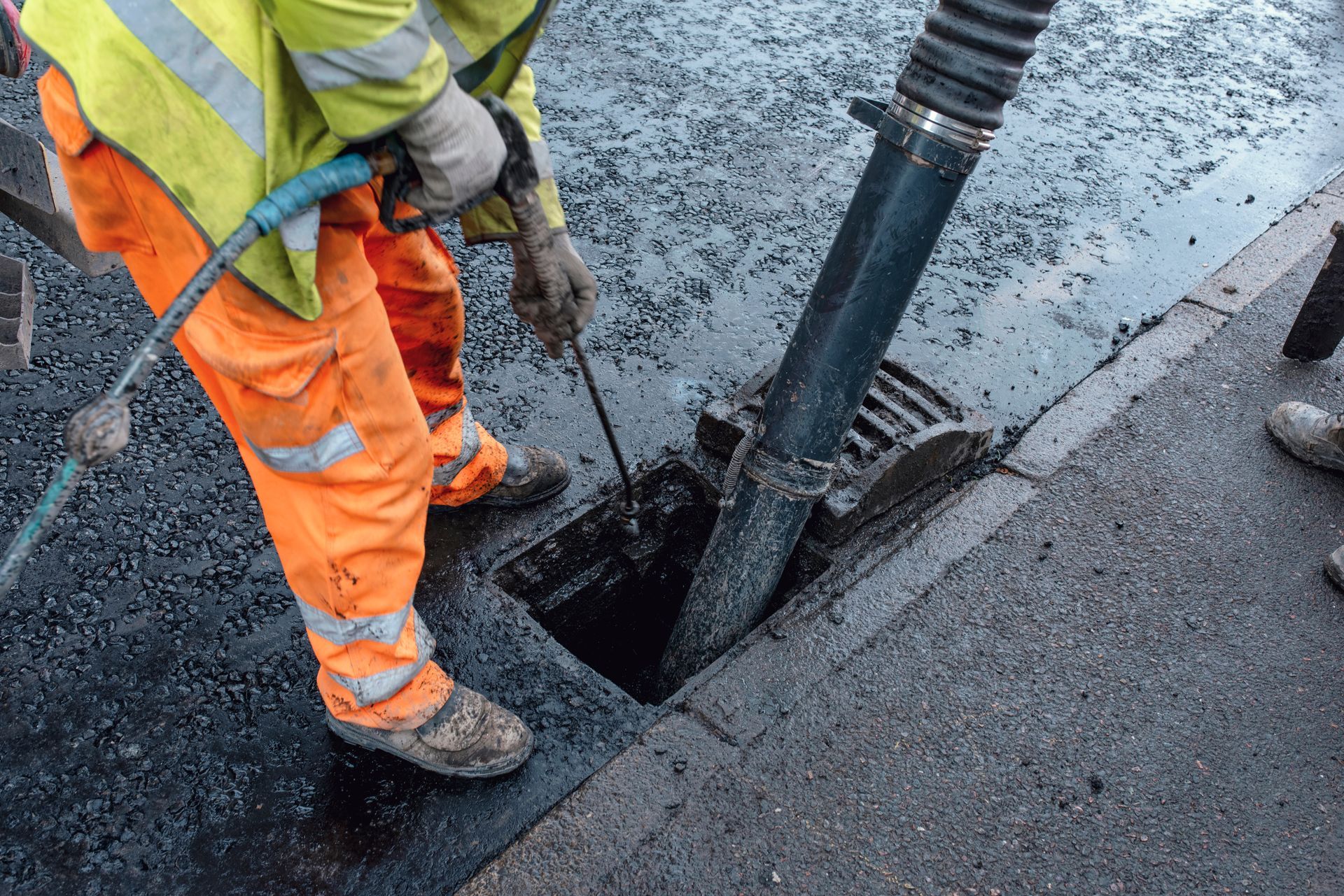Construction worker operates a vacuum truck to clear debris from a storm drain.