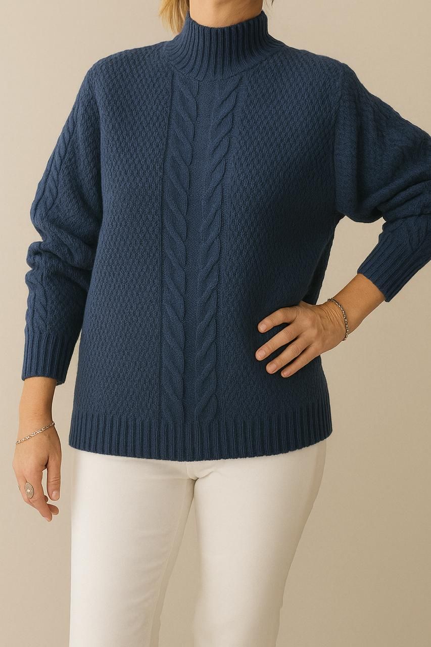 Mujer con un suéter de punto azul y pantalones blancos, posando con la mano en la cadera.
