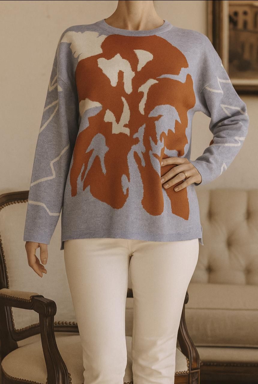 Mujer vistiendo un suéter azul claro con un diseño de color óxido, combinado con pantalones blancos.