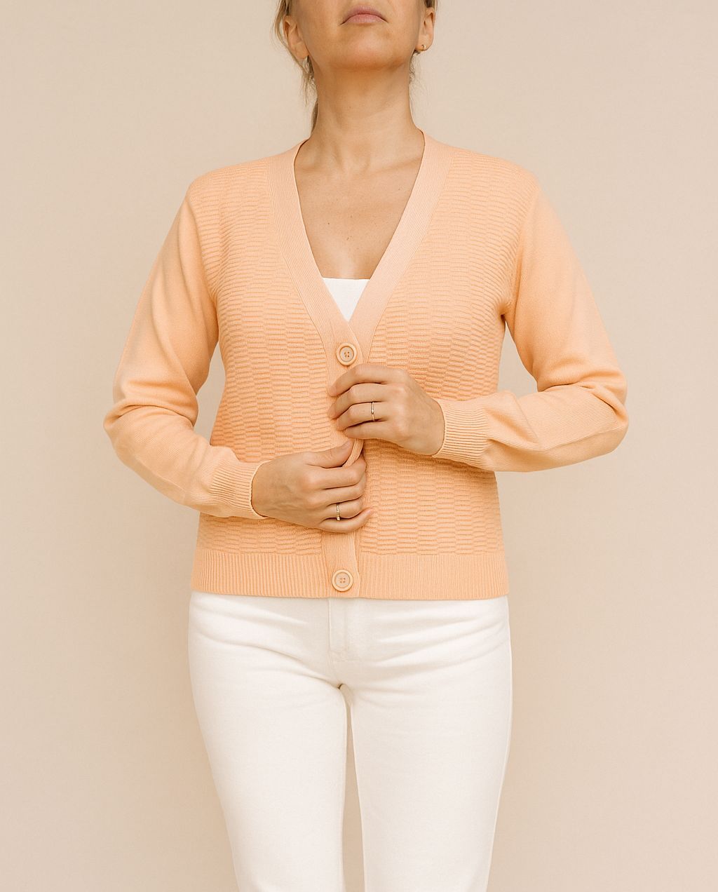 Mujer con cárdigan color melocotón y pantalones blancos, abotonándolos.