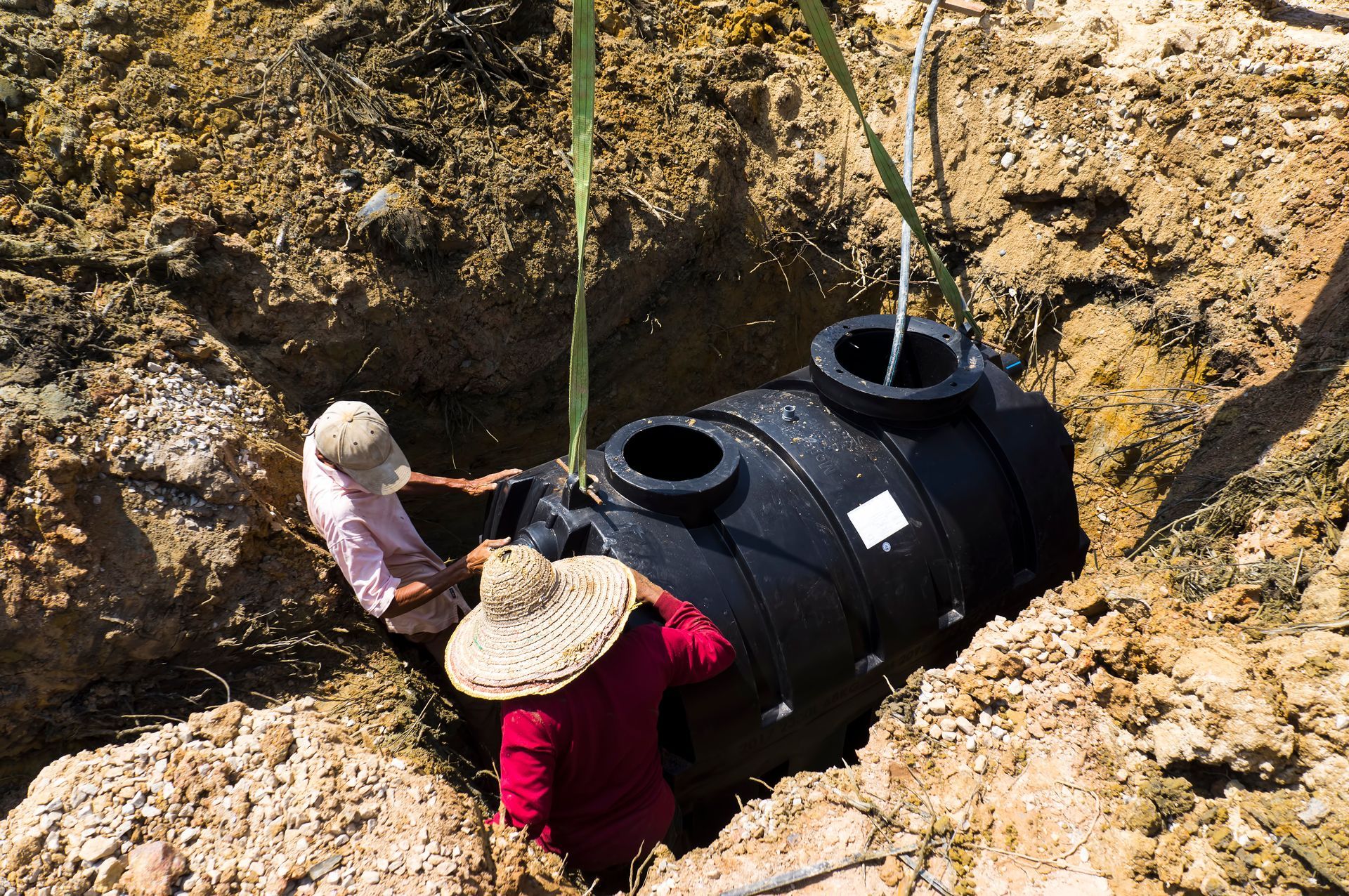 A worker is using a vacuum hose to clear a hole beside a concrete slab in a grassy area.