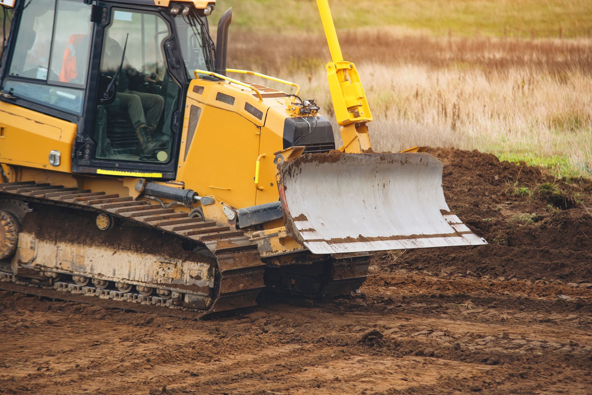 Yellow bulldozer scraping dirt in a muddy field with a raised front blade.