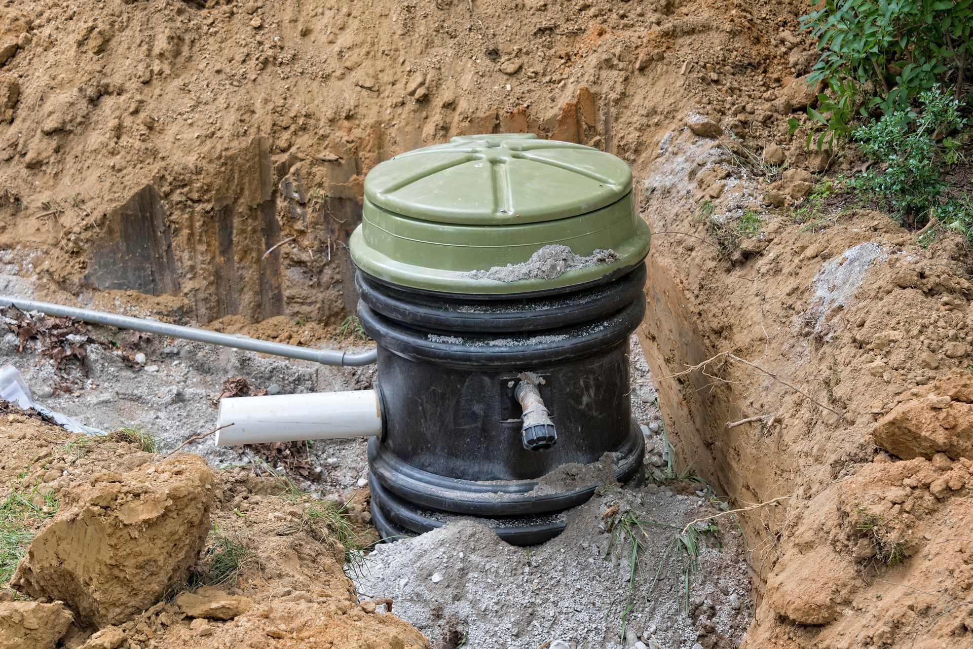 A green utility manhole chamber in a dirt excavation site with pipes attached.