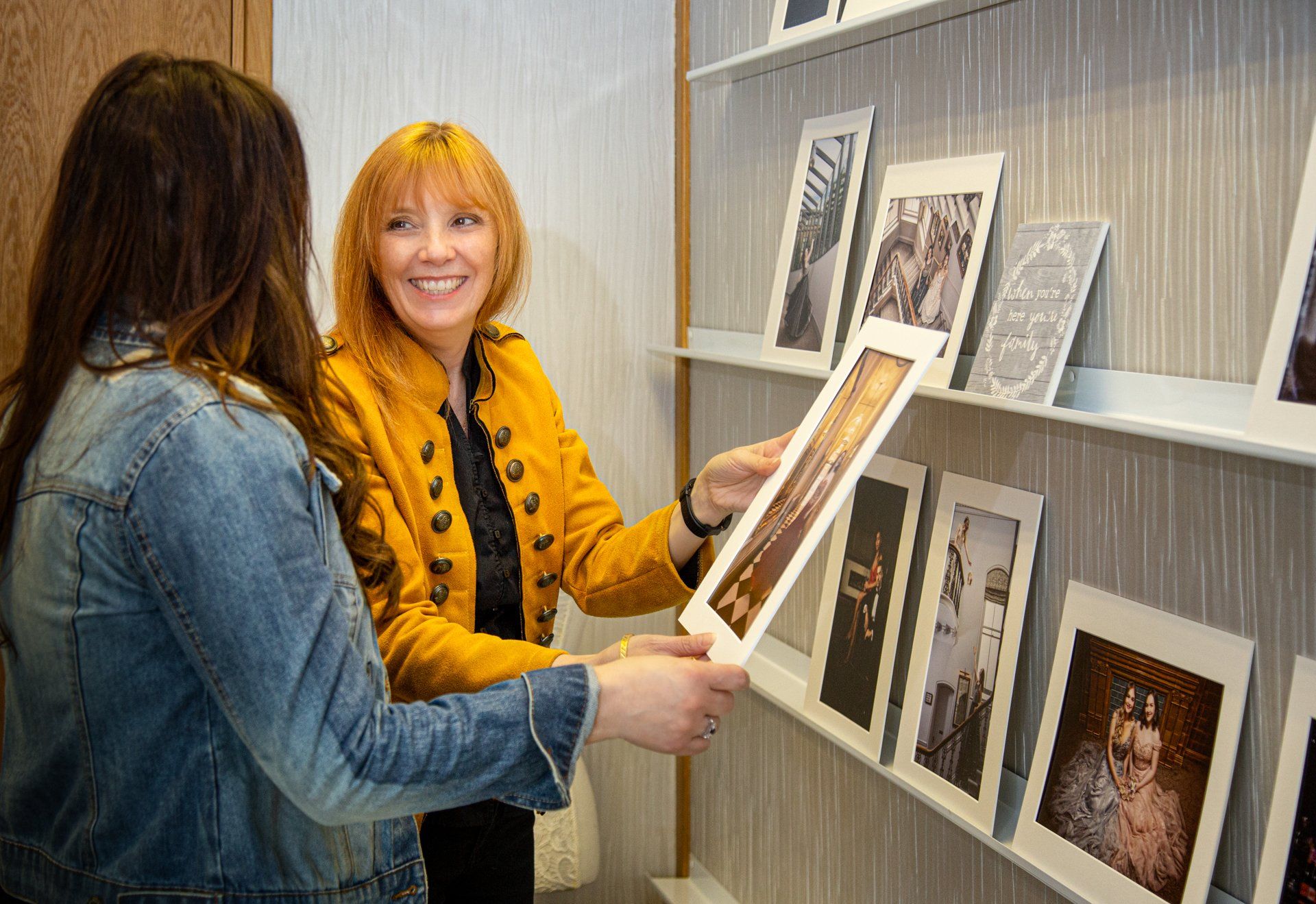 Two women are looking at pictures on a shelf in a store.