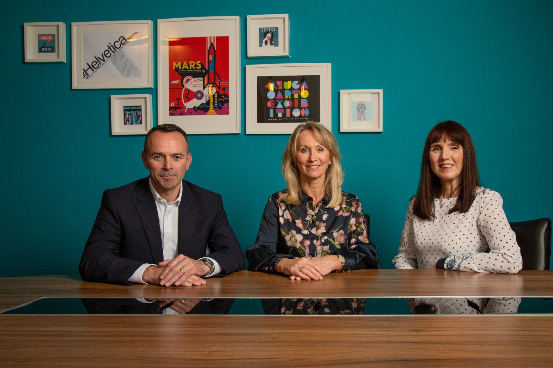 Three people are sitting at a table in front of a blue wall.