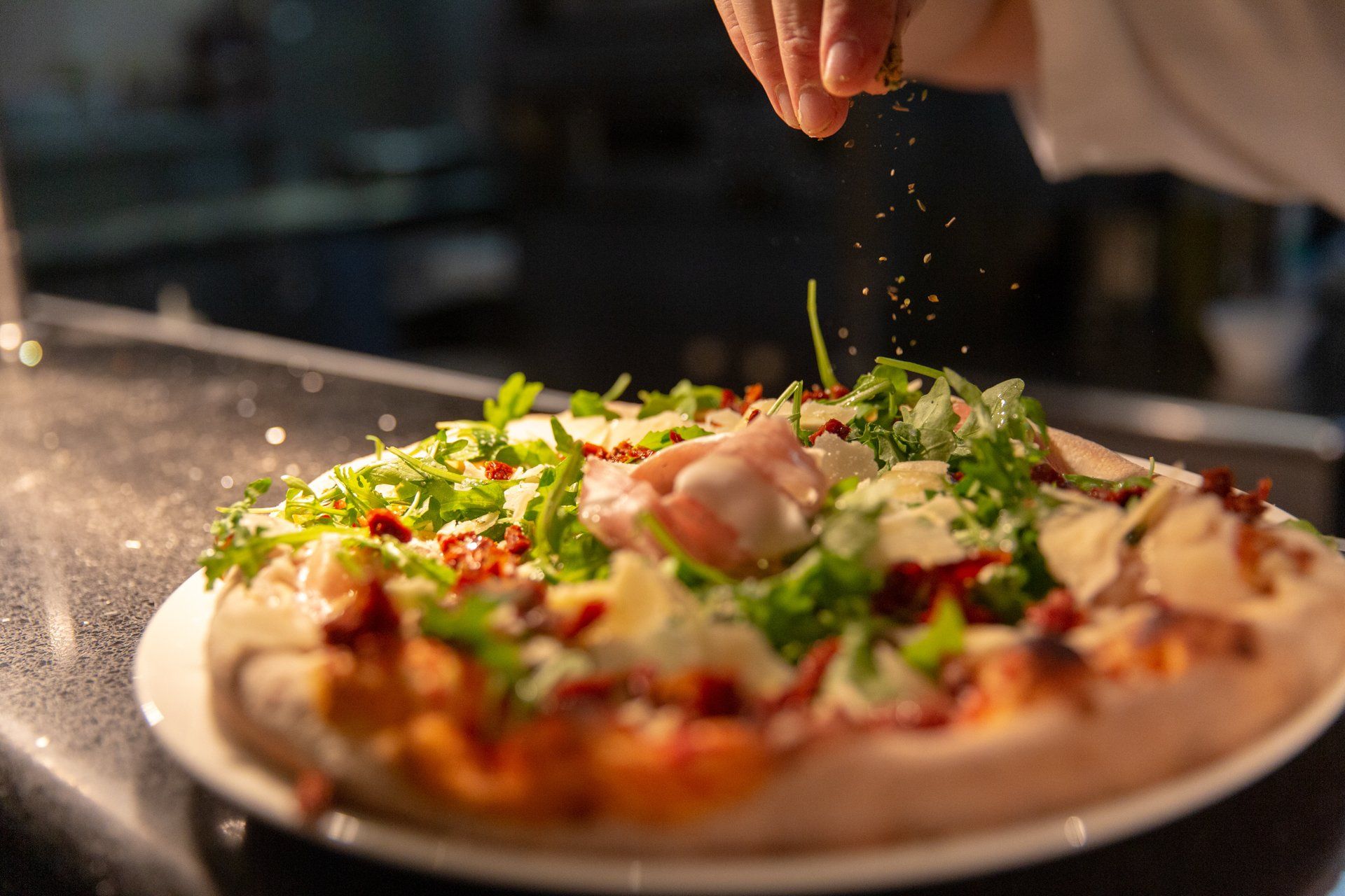 A person is sprinkling salt on a pizza on a plate.
