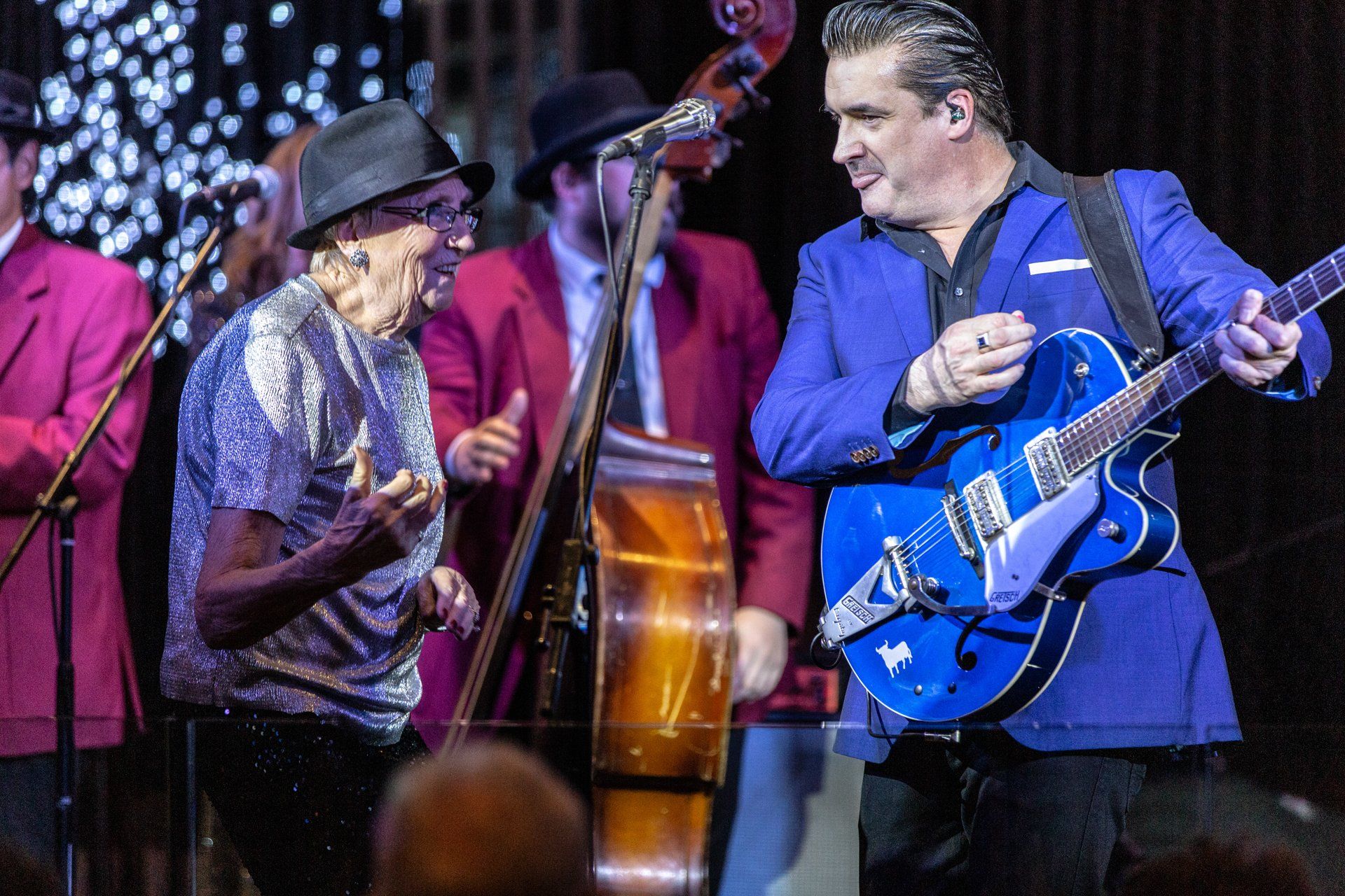 A man in a blue suit is playing a blue guitar on stage.