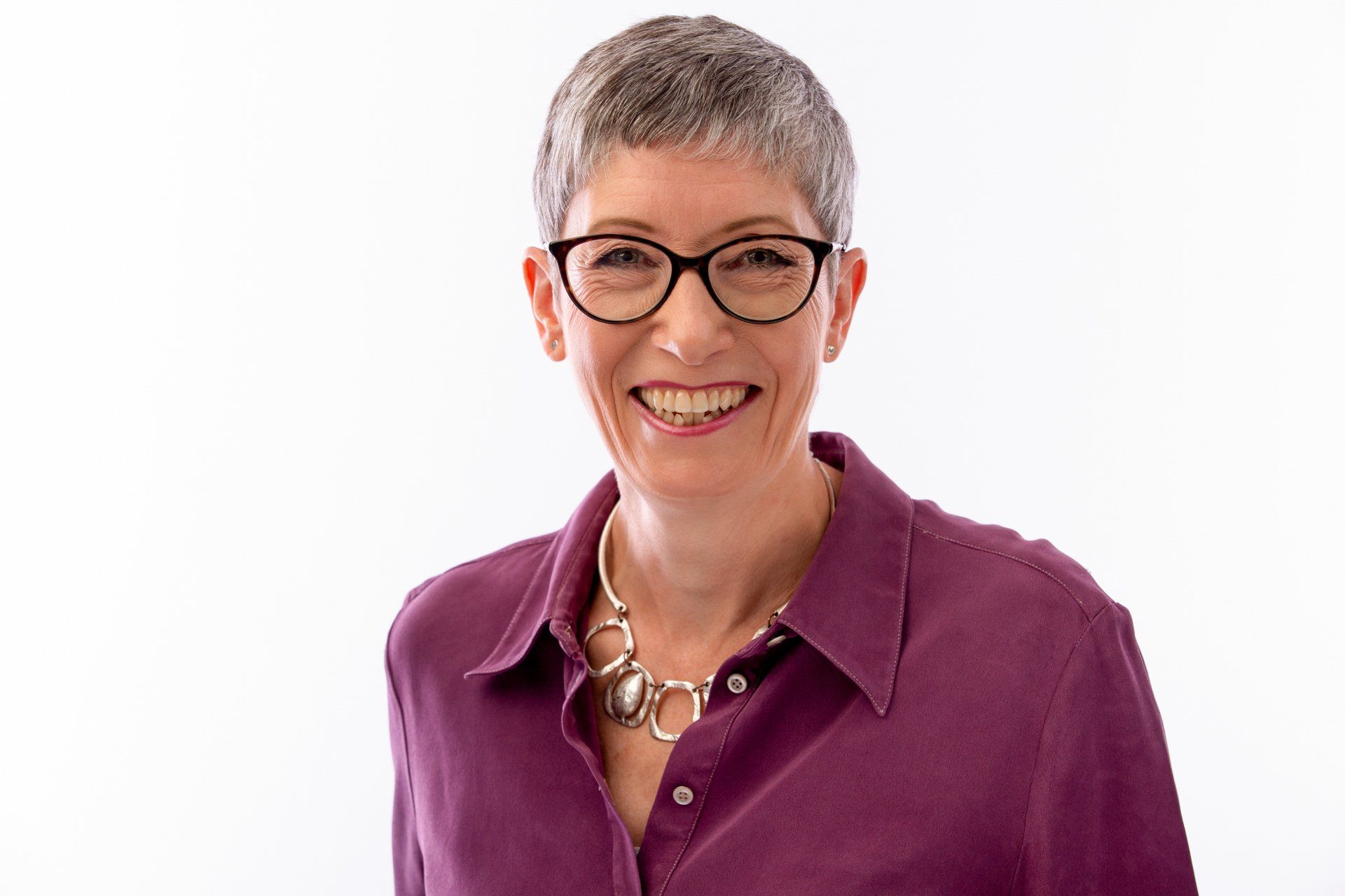 A woman wearing glasses and a purple shirt is smiling for the camera.
