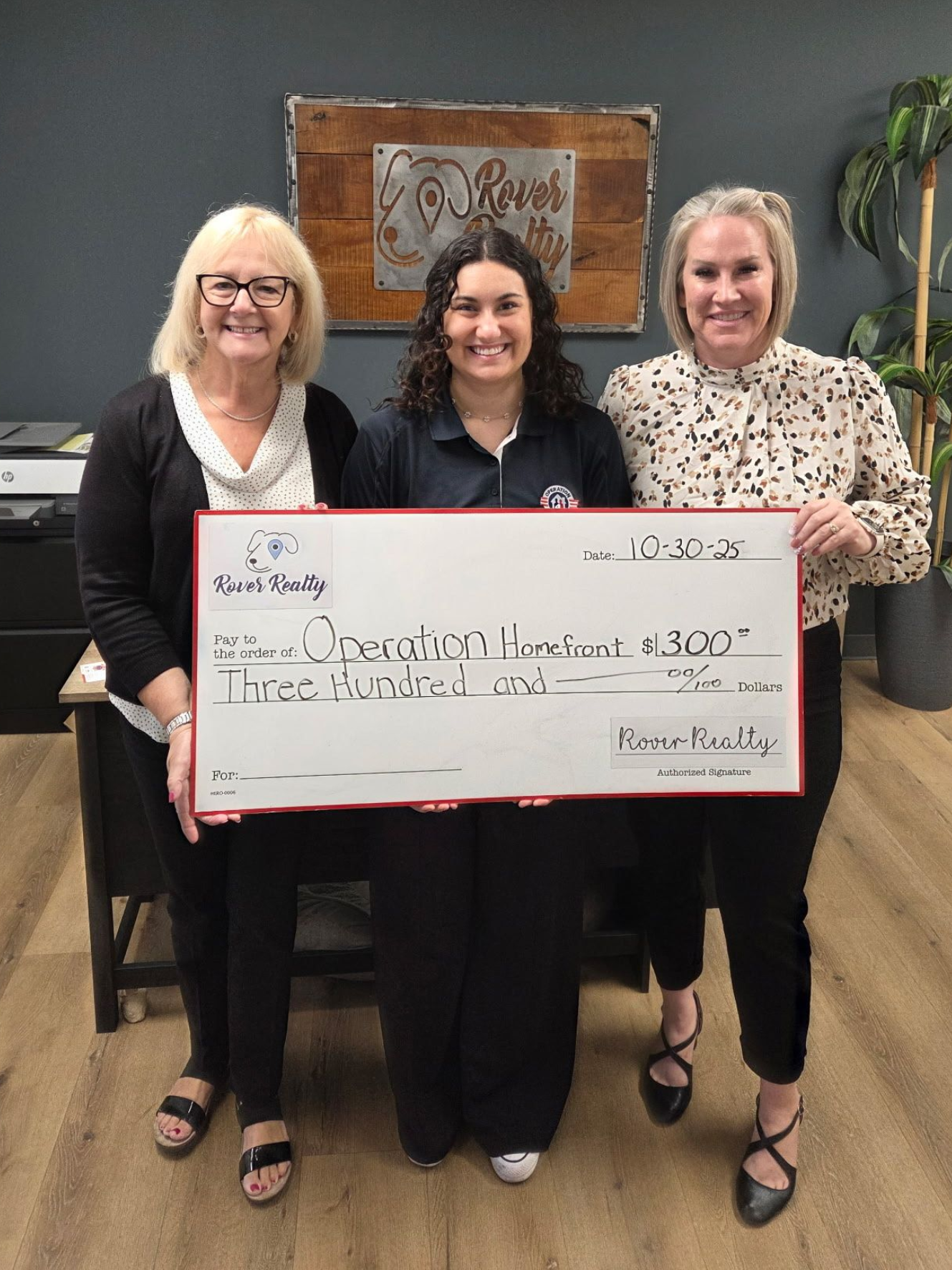 Three women holding a large ceremonial check in an office