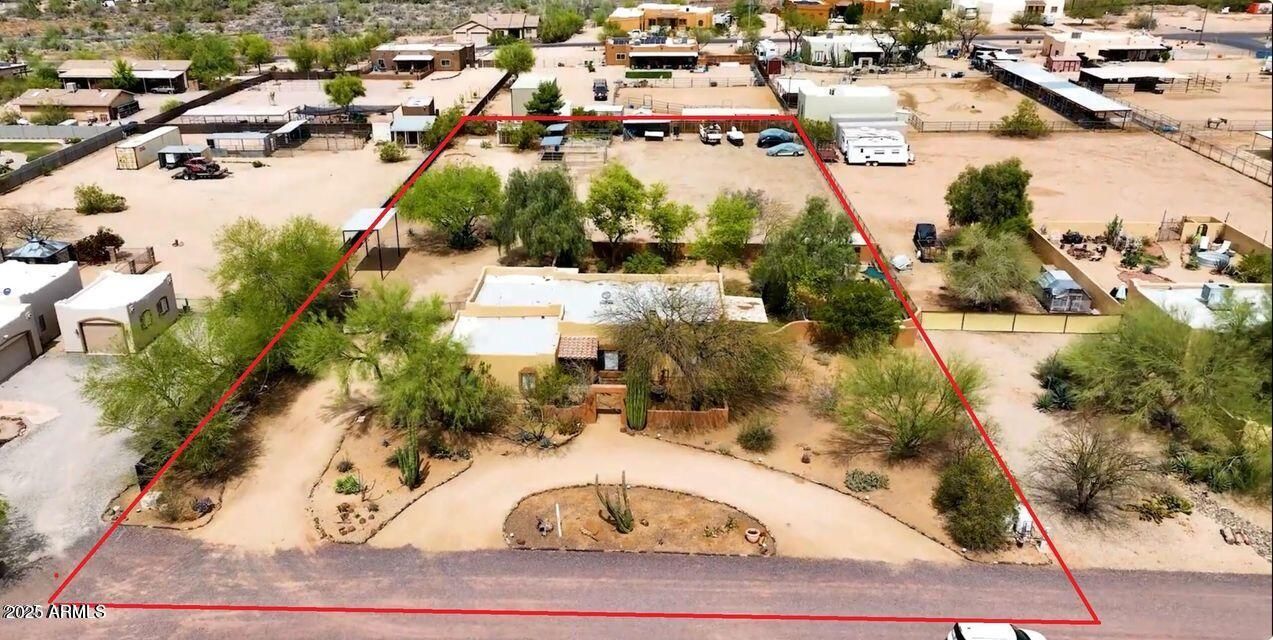 Aerial view of a desert neighborhood with homes, trees, and dirt roads inside a red outlined lot.