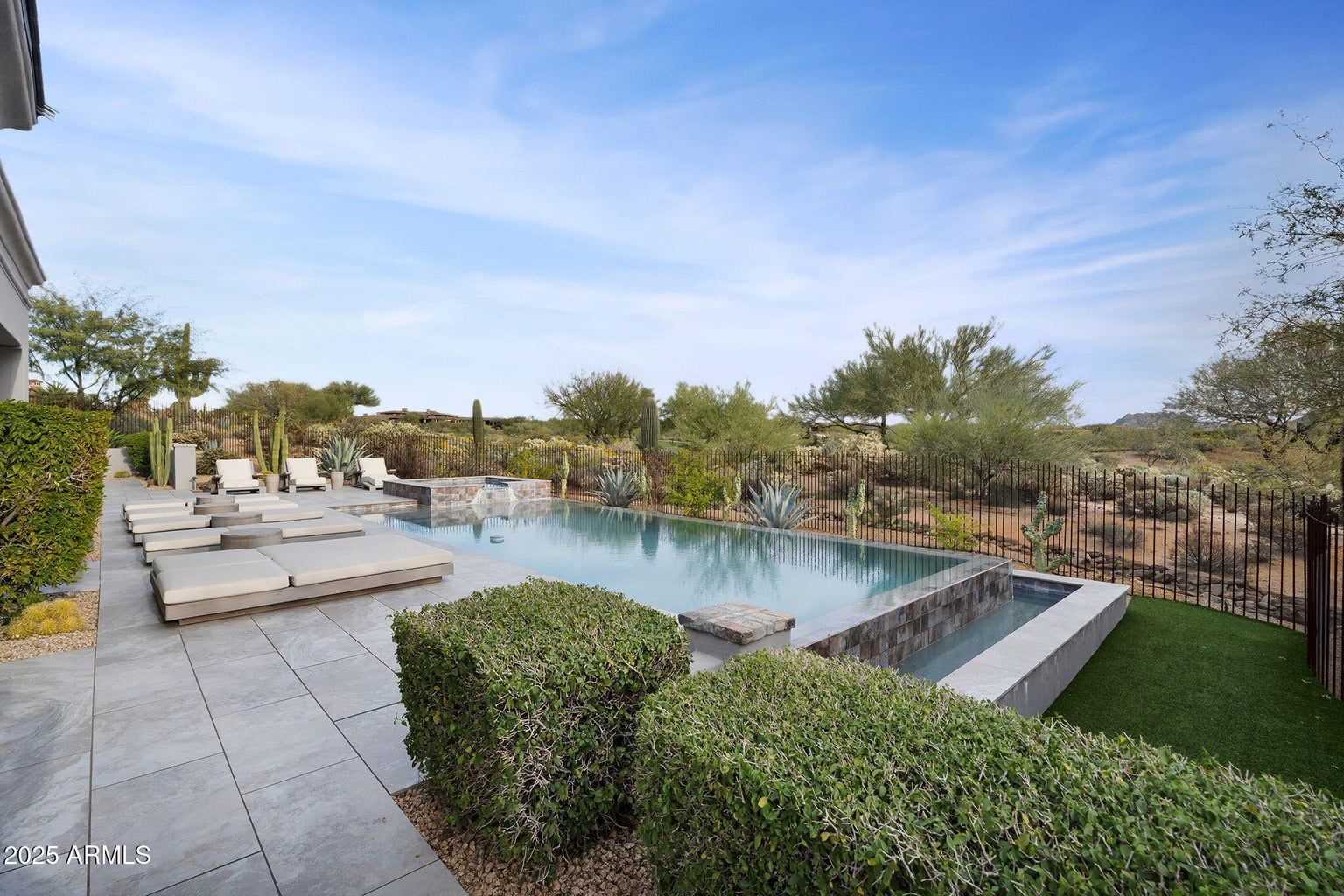 Luxury backyard pool with loungers, hedges, and palm trees under a clear blue sky