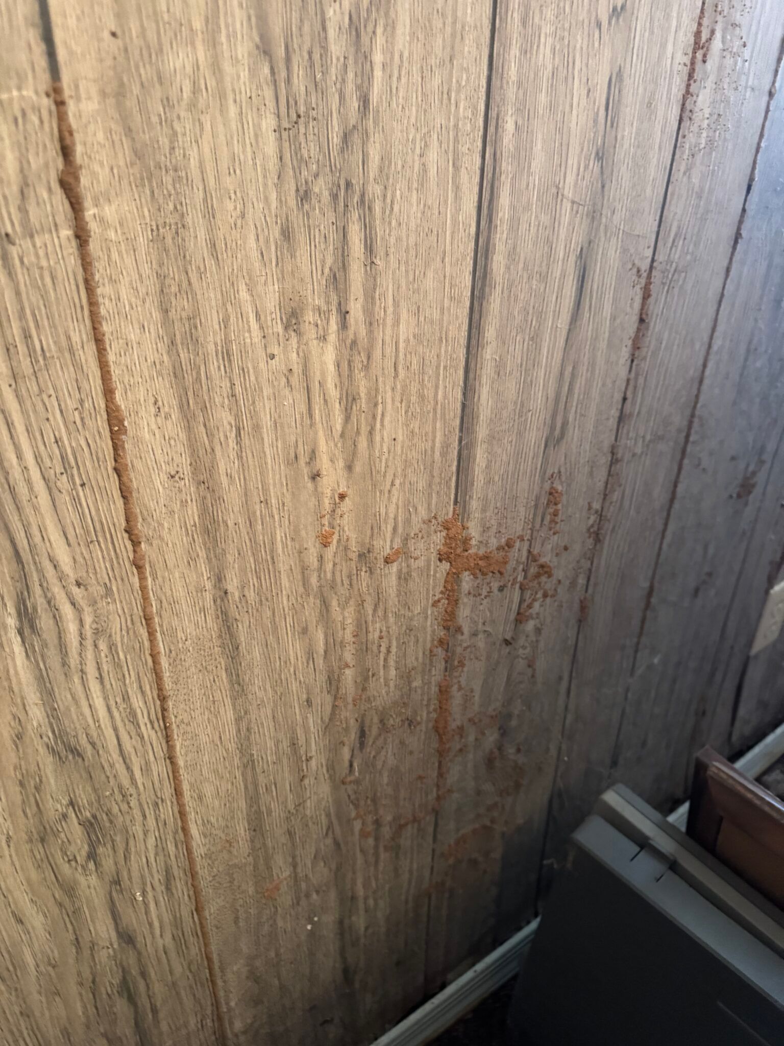 Weathered wooden fence with a rust-colored stain, next to part of a metal object.