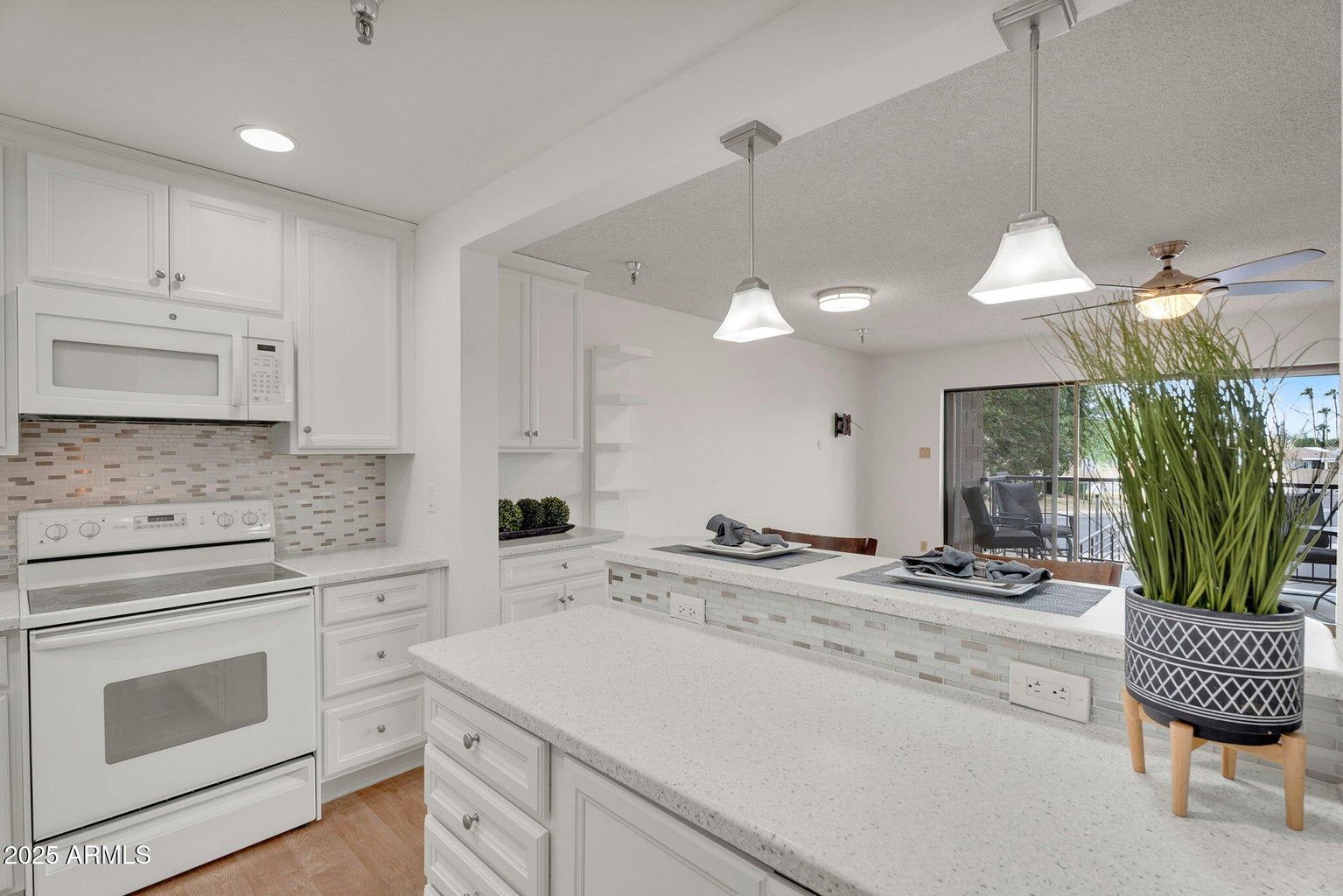 Bright white modern kitchen with island, pendant lights, and a potted plant on the counter.