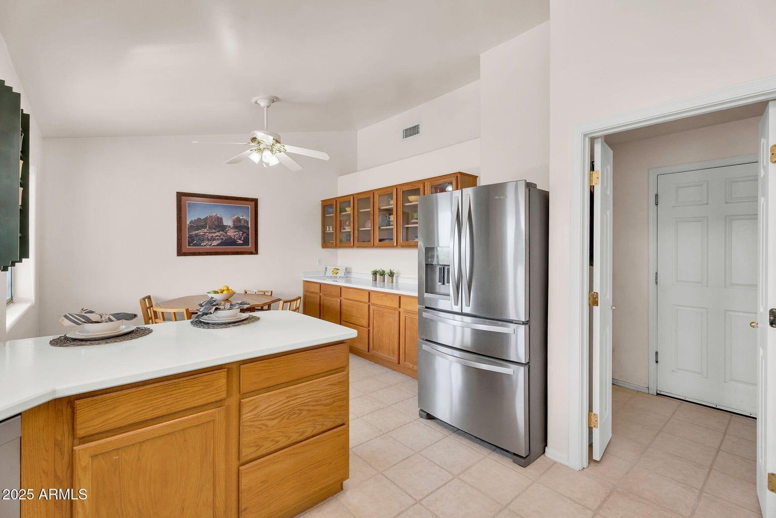 Bright kitchen with wooden cabinets, stainless steel fridge, white island, and tiled floor