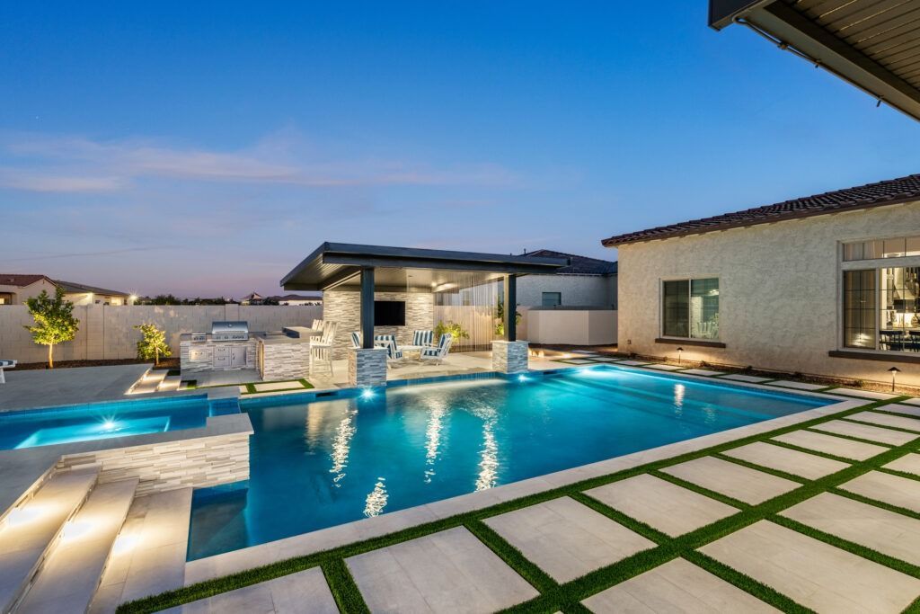 Modern villa courtyard with illuminated swimming pool at dusk and stone-tiled patio