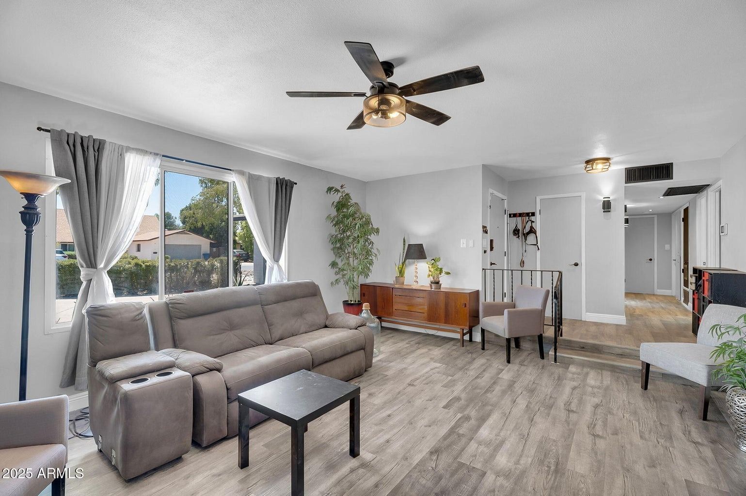 Bright living room with gray sofa, large windows, ceiling fans, and wood-look flooring