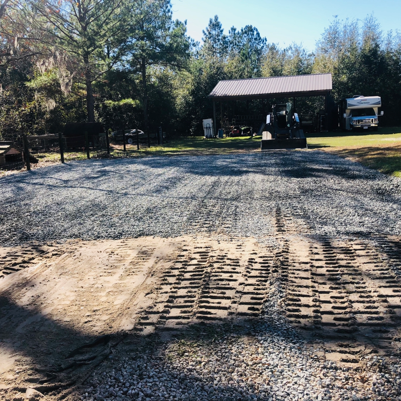 Gravel driveway with machine tracks. Shed, trees, and RV in the background. Sunny day.