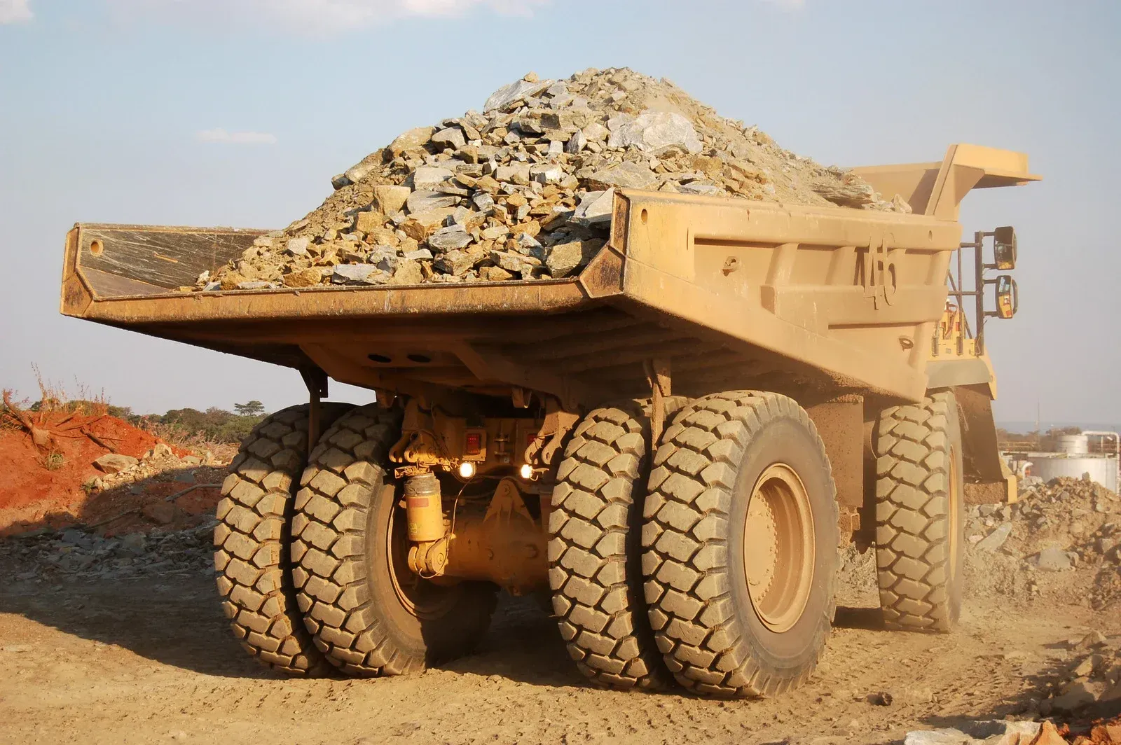 Yellow excavator loading a red dump truck with dirt on a construction site under a blue sky.