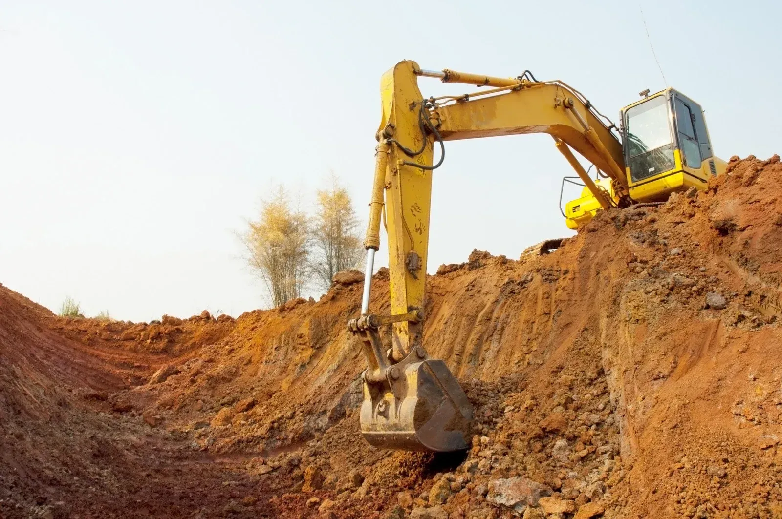 Yellow excavator digging in red soil on a sunny day.