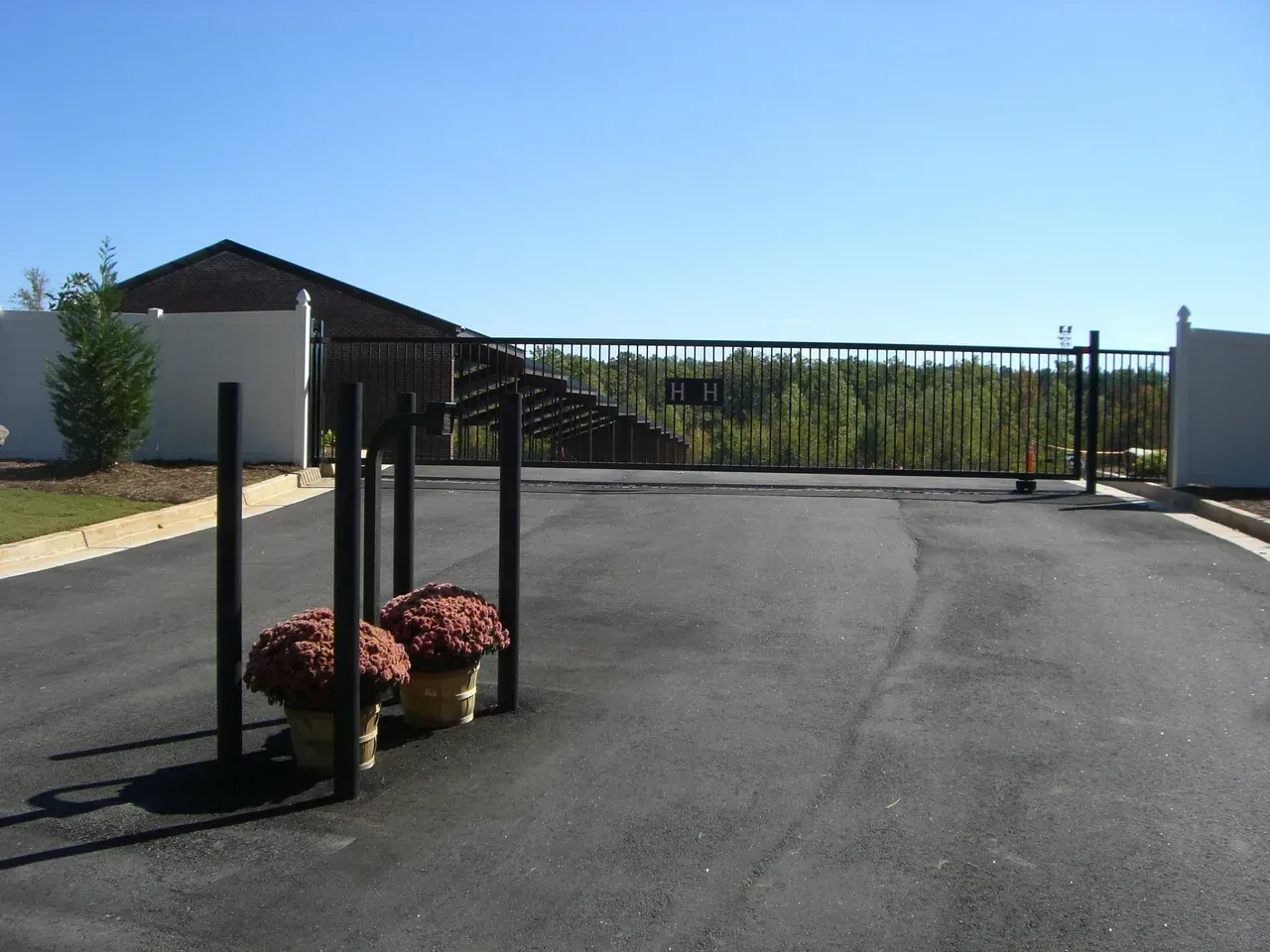 Black gated entrance to a property, with flower pots in the foreground and a house visible in the background.