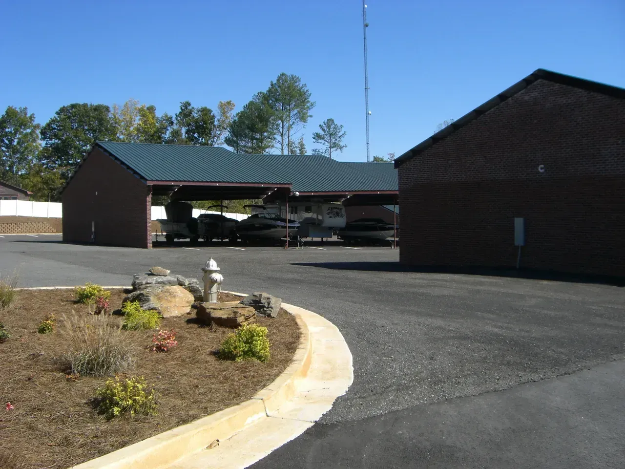 Boat storage sheds with a dark green roof, a red brick building, and a small garden with a fire hydrant.