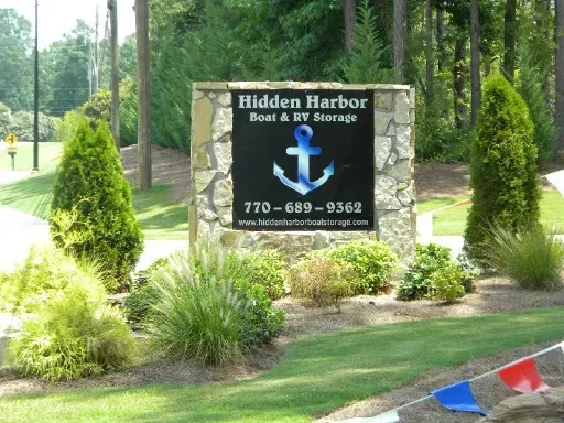 Sign for Hidden Harbor Boat & RV Storage, with an anchor logo on a black background, surrounded by landscaping.