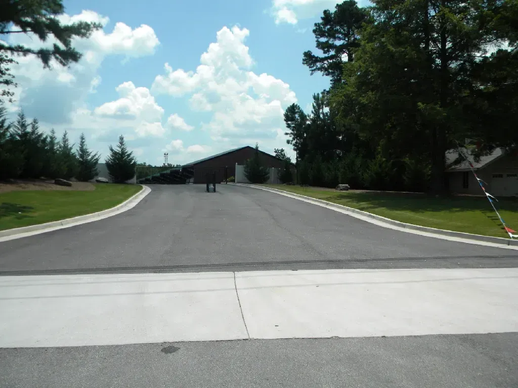 Asphalt road leading to a dark brown building, under a blue sky with puffy white clouds.
