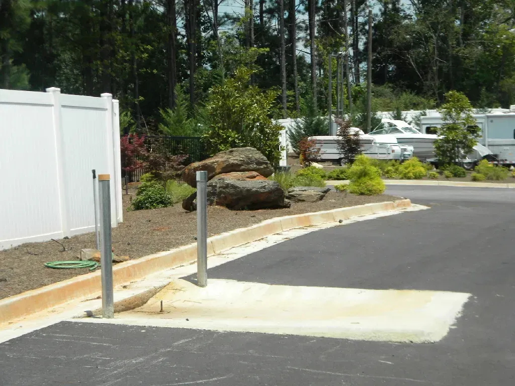 Concrete pad and two metal posts in front of a white fence and landscaped area with RVs in the background.